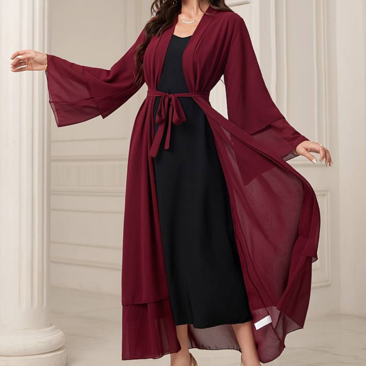 Frau in eleganter, burgunderroter Chiffon-Cardigan mit Gürtel über schwarzem Kleid, stehend in stilvollem, klassischem Innenraum.