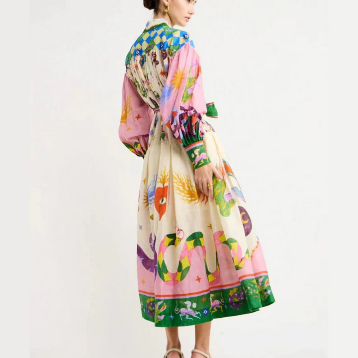 Frau in buntem, langem Kleid mit auffälligem Muster aus Schlangen und Pflanzen, steht seitlich. Modetrend, farbenfrohes Design, Damenmode.