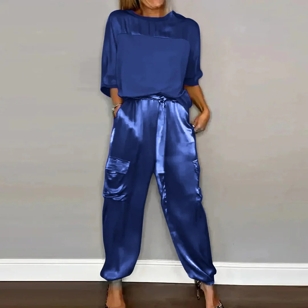 Frau in blauer Satinbluse und Satinjogginghose, lässiger Look, modische Damenbekleidung, eleganter Stil, bequeme Freizeitmode.