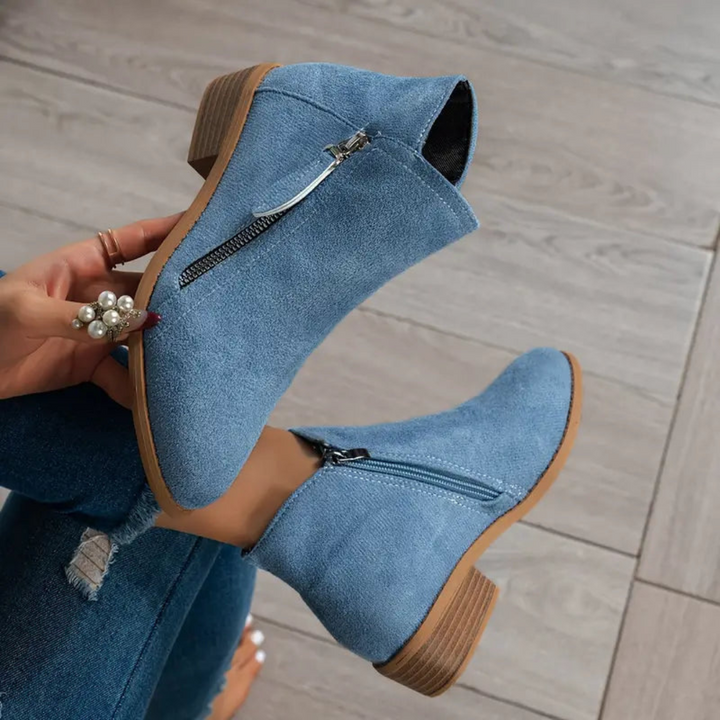 Blaue Damen-Stiefeletten mit Reißverschluss, flachem Absatz und Holzsohle auf Holzboden. Modische Herbstschuhe, bequem und stilvoll.