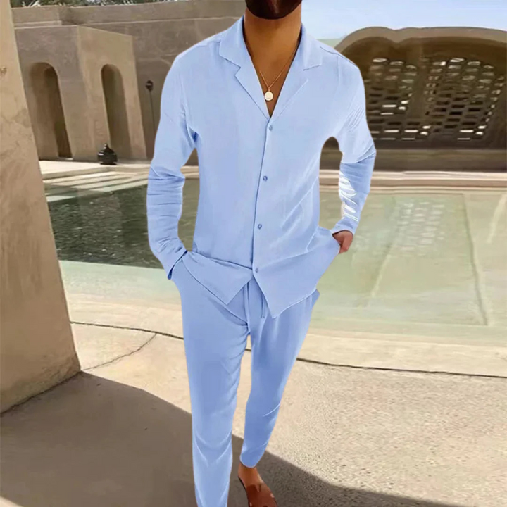 Mann in hellblauem Pyjama-Set aus Baumwolle, steht vor modernem Gebäude mit Pool. Bequeme Nachtwäsche, ideal für Sommernächte.