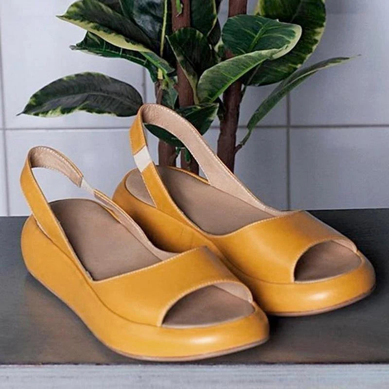 Gelbe Damen-Slingback-Sandalen aus Leder auf grauem Tisch, mit grüner Pflanze im Hintergrund. Bequeme Sommerschuhe, modisch und elegant.