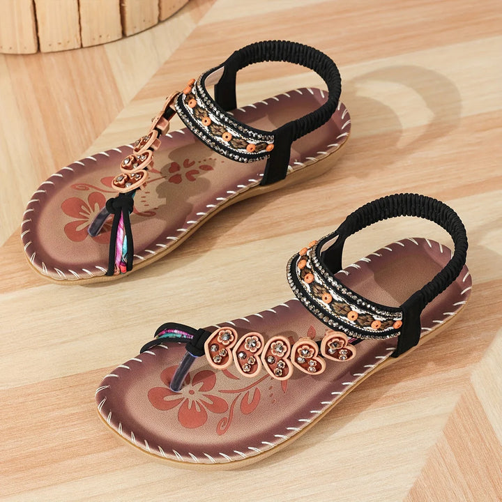 Damen-Sandalen mit Blumenmuster, Perlenverzierung und elastischem Riemen auf Holzoptik-Boden. Ideal für Sommermode und Freizeitkleidung.