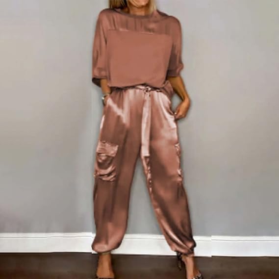 Frau in eleganter, rosafarbener Satin-Hose und passendem Oberteil vor grauer Wand. Modetrend, Damenbekleidung, stilvoller Look.