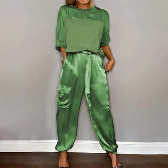 Frau in grüner Satin-Hose und passendem Oberteil vor grauer Wand. Modetrend, elegante Damenbekleidung, stilvolle Freizeitmode.