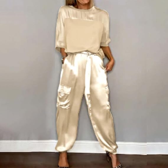 Dame in eleganter, cremefarbener Satinbluse und passender Hose, posiert vor grauer Wand. Modetrend, stilvolle Damenbekleidung, Satin-Outfit.