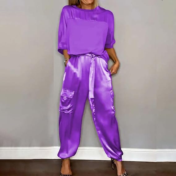 Frau in lila Satin-Set mit lockerem Oberteil und Jogginghose, modisch und elegant, vor grauer Wand. Trendige Damenmode, stilvoll und modern.