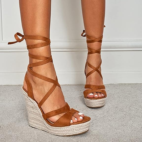 Braune Keilsandaletten mit Schnürung, Espadrille-Design und geflochtener Sohle auf grauem Teppich. Modische Sommerschuhe für Damen.