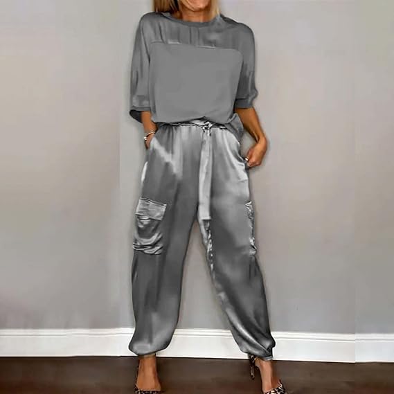 Frau in grauem Satin-Outfit, bestehend aus lockerem Oberteil und Cargo-Hose, steht vor grauer Wand. Modetrend, eleganter Look, Damenmode.