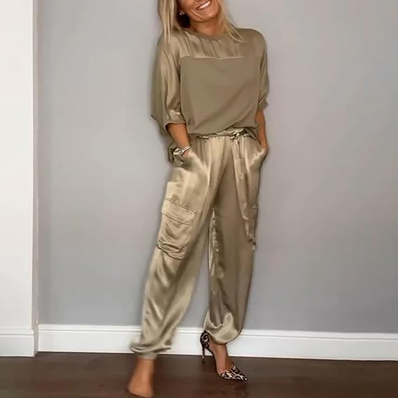 Frau in eleganter, beiger Satin-Hose und Bluse, lächelt vor grauer Wand. Modetrend, Damenmode, stilvolle Freizeitkleidung, Satin-Outfit.