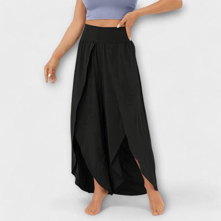 Frau trägt schwarzen Maxirock mit hohem Bund und seitlichem Schlitz, kombiniert mit lila Crop-Top. Modetrend, Damenbekleidung, Sommeroutfit.