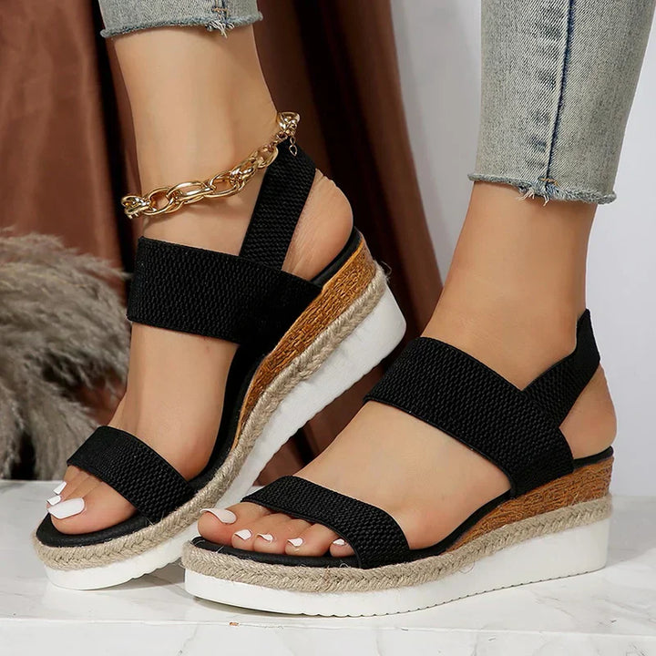 Schwarze Damen-Sandalen mit Keilabsatz, geflochtenem Juteband und weißer Sohle, getragen mit Jeans. Modische Sommer-Schuhe für Damen.