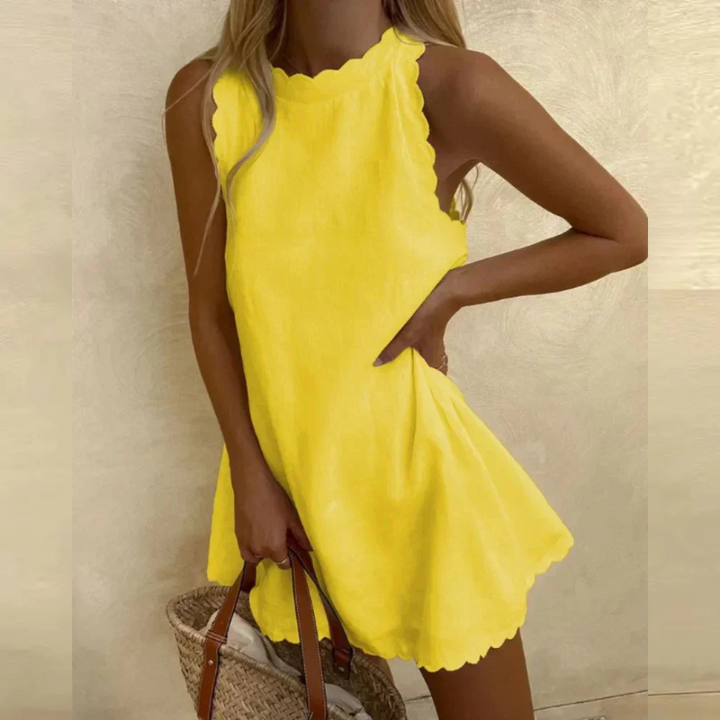 Blonde Frau in gelbem Sommerkleid mit gewelltem Saum, hält eine Strohtasche. Perfekt für Strandmode, Sommeroutfit, Freizeitkleidung.