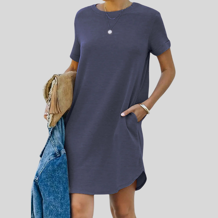 Frau in dunkelblauem T-Shirt-Kleid mit Taschen, hält eine Jeansjacke und eine beige Tasche. Modetrend, lässiger Stil, Damenbekleidung.