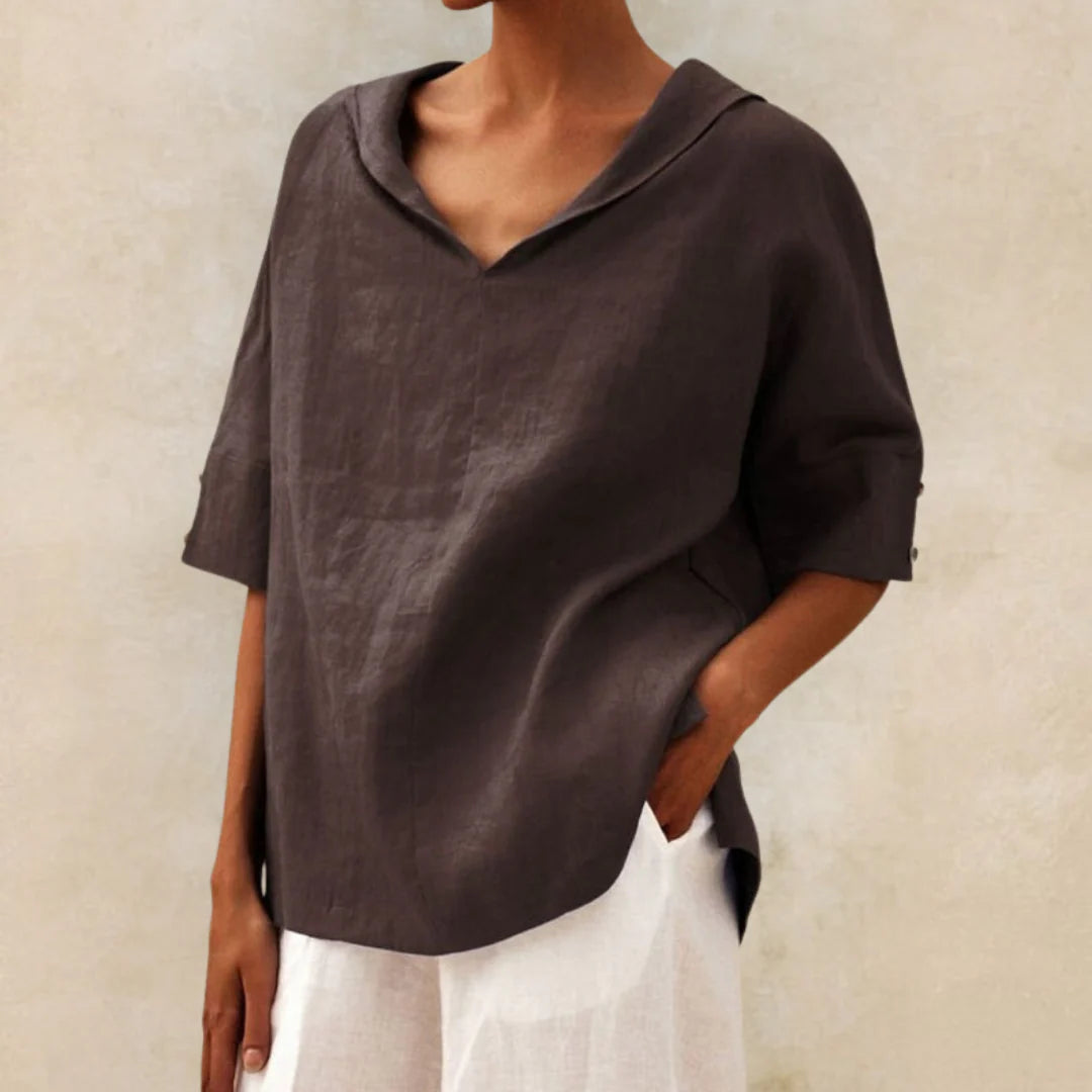 Dunkelbraune Leinenbluse mit V-Ausschnitt und halblangen Ärmeln, kombiniert mit weißer Hose. Elegante, lässige Damenmode aus Naturmaterialien.