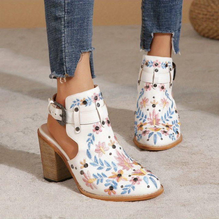 Weiße, bestickte Damenstiefeletten mit Blumenmuster und Blockabsatz, kombiniert mit zerrissenen Jeans. Modische Schuhe für den Herbst.