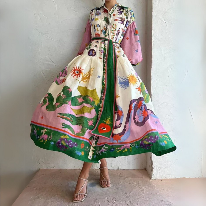 Buntes Maxikleid mit langen Ärmeln, verziert mit Schlangen- und Sonnenmotiven, getragen von einer Frau in Sandalen vor einer weißen Wand.