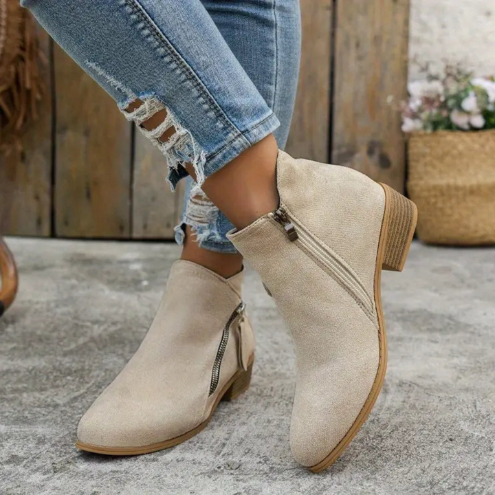 Beige Damen-Stiefeletten mit Reißverschluss, kombiniert mit zerrissenen Jeans. Modische Herbstschuhe, ideal für lässige Outfits.