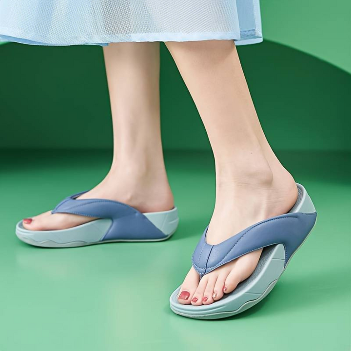Damenfüße in blauen ergonomischen Sandalen auf grünem Boden. Bequeme, modische Sommerschuhe, ideal für Freizeit und Strand.