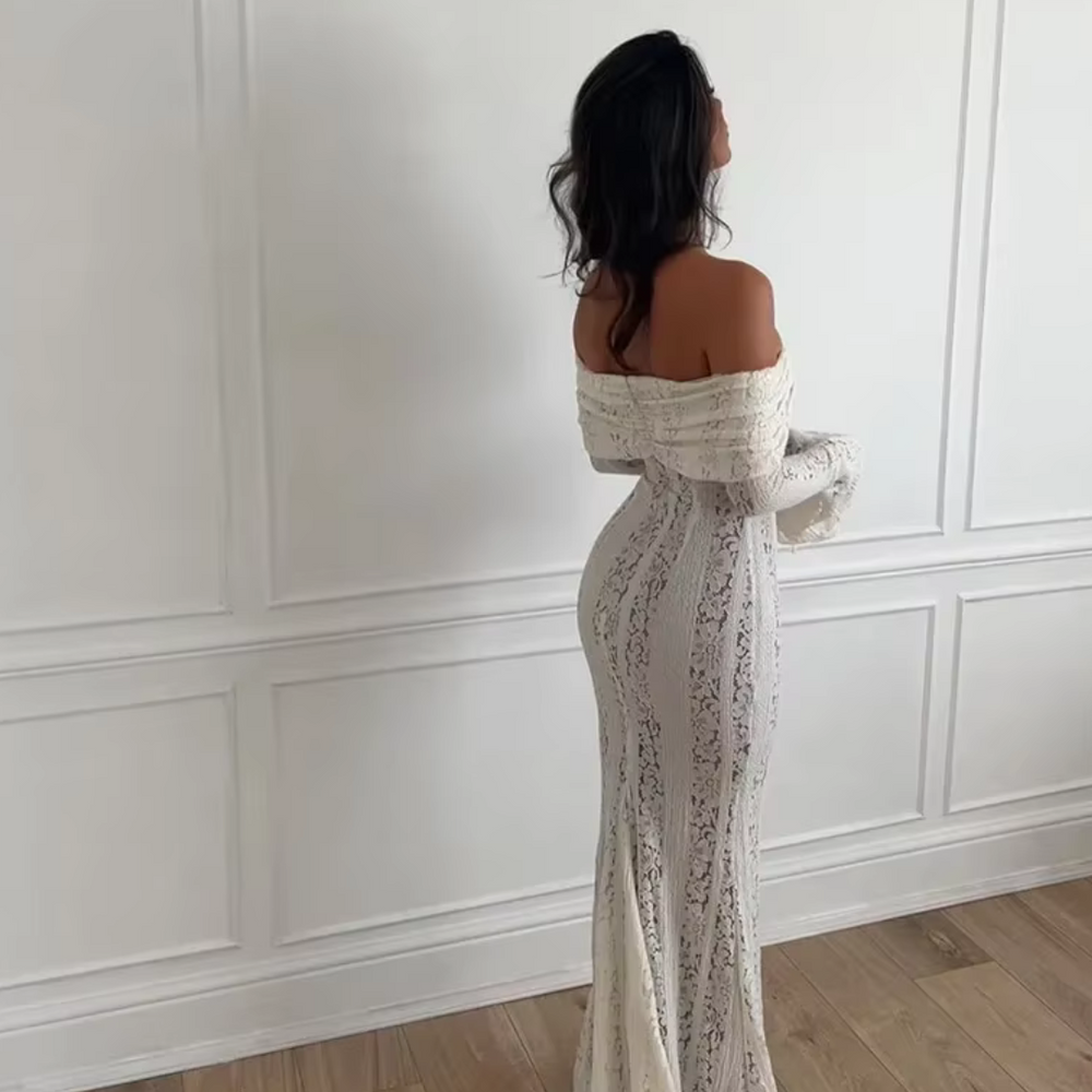 Frau in eleganter, schulterfreier Spitzenkleid, steht vor weißer Wand. Mode, Abendkleid, stilvoll, elegant, Damenmode, Spitzenkleid, schulterfrei.