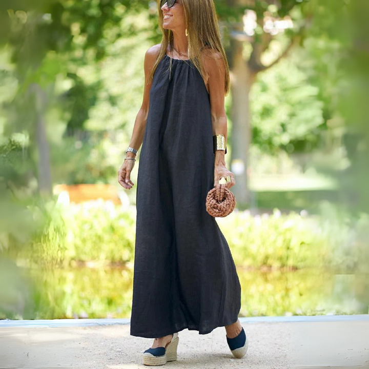 Frau in schwarzem Maxikleid, trägt Sonnenbrille und Keilsandalen, hält runde Handtasche. Sommermode, eleganter Look im Freien.