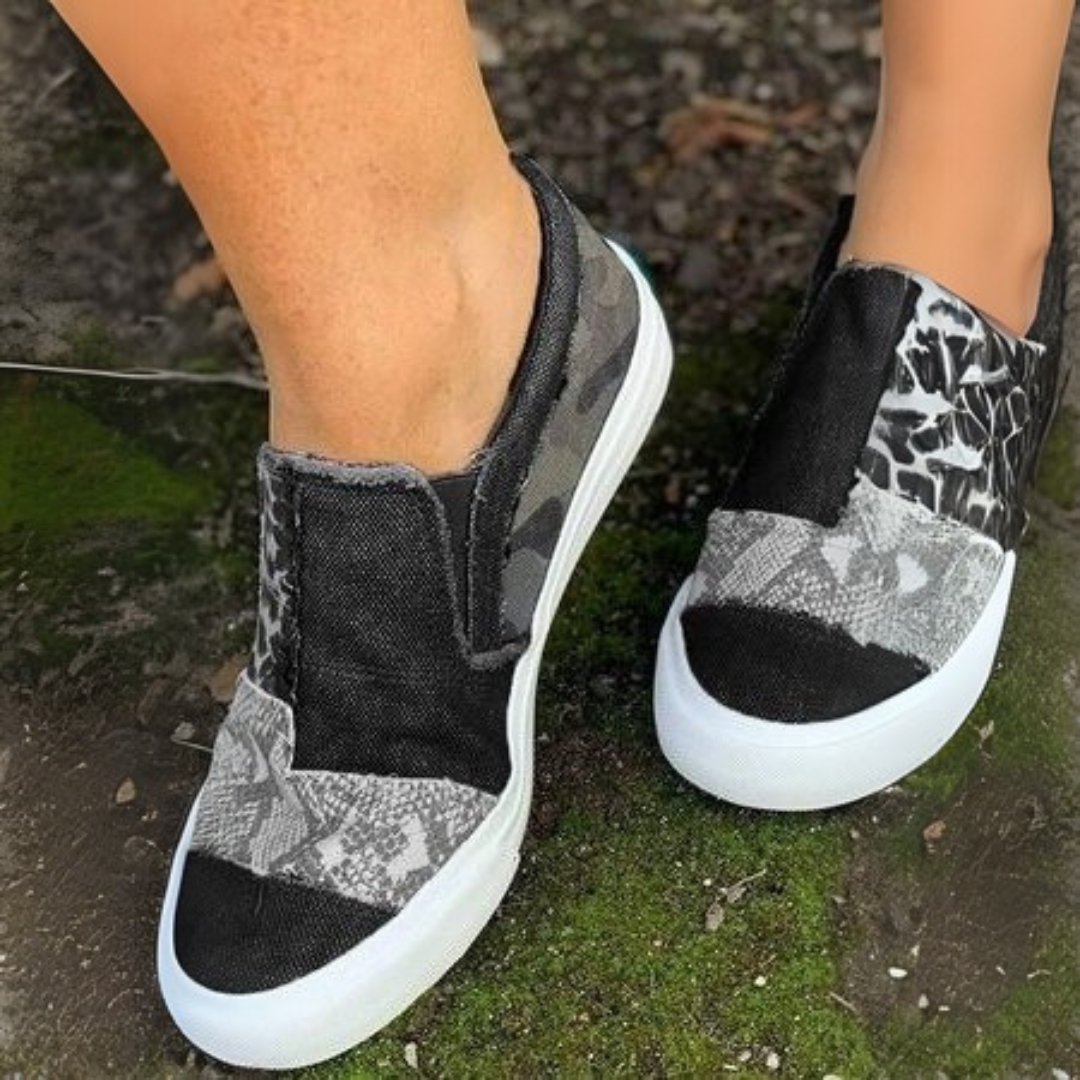 Schwarze und graue Slip-On-Sneaker mit Camouflage- und Leopardenmuster auf moosbedecktem Boden. Modische Freizeitschuhe für Damen.