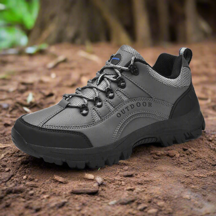 Grauer Outdoor-Wanderschuh auf Waldboden, robustes Design mit rutschfester Sohle, ideal für Trekking und Naturabenteuer.