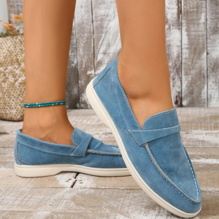 Blaue Wildleder-Loafer für Damen auf Holzboden, modisch und bequem, ideal für Sommeroutfits. Perfekte Freizeitschuhe mit weißer Sohle.