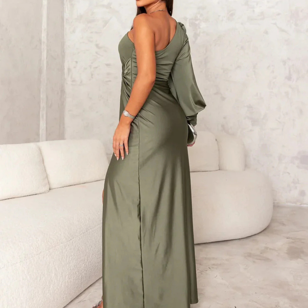 Frau in elegantem, olivgrünem, einärmligem Abendkleid posiert vor cremefarbenem Sofa. Modetrend, Abendmode, stilvolles Design.