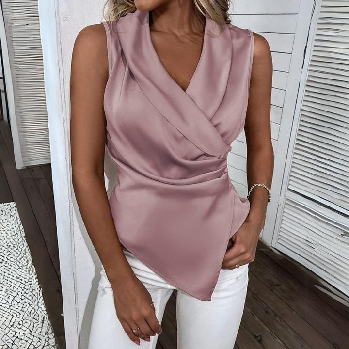 Frau in eleganter, ärmelloser, rosa Satinbluse mit V-Ausschnitt und Wickeldesign, kombiniert mit weißen Jeans. Perfekt für stilvolle Sommermode.