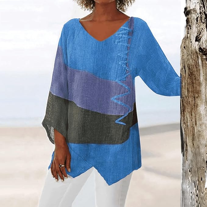 Frau in blau-lila gestreifter Tunika am Strand, lehnt an Baumstamm. Sommermode, lässiger Stil, V-Ausschnitt, weite Ärmel. Ideal für Strandspaziergänge.