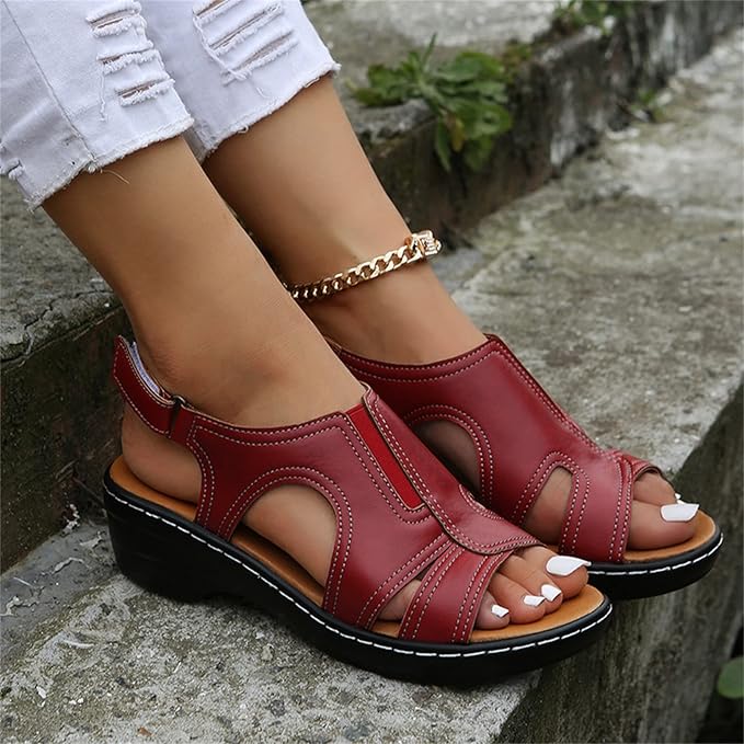 Rote Sandalen mit Keilabsatz, getragen von einer Person mit weißer Hose auf einer Steintreppe. Modische Sommerschuhe, bequem und stilvoll.