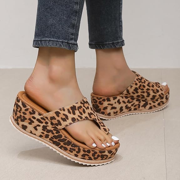 Frau trägt Leopardenmuster-Sandalen mit Keilabsatz, kombiniert mit dunkelblauen Jeans. Modische Sommerschuhe, bequem und stilvoll.