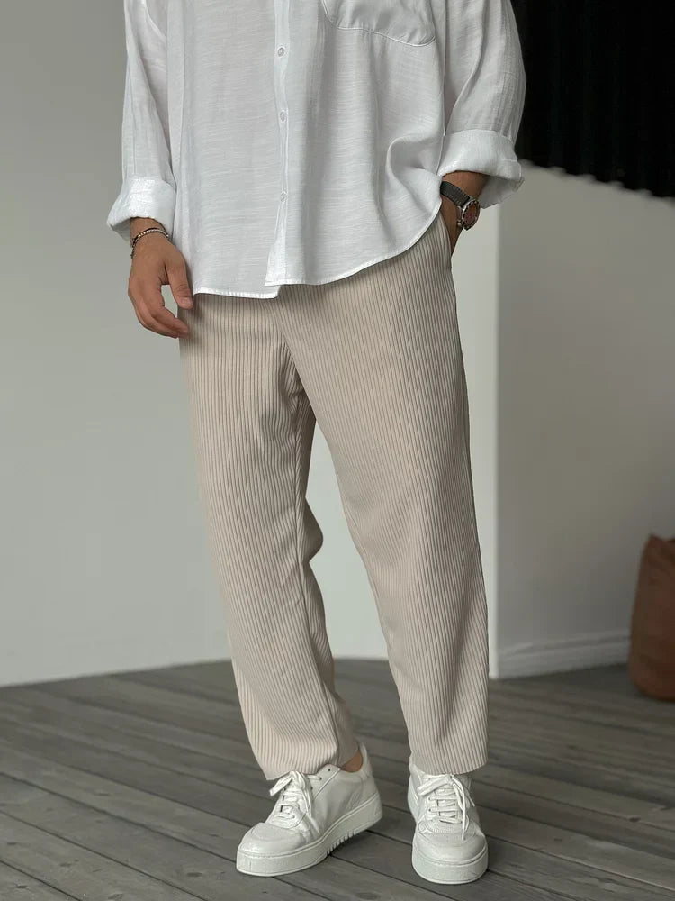 Weiße Hemd und beige, gerippte Hose, kombiniert mit weißen Sneakers auf Holzboden. Modischer Herren-Look, lässig und stilvoll.