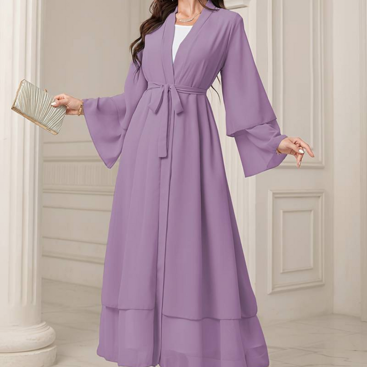 Lila Maxikleid mit Gürtel, langen Ärmeln und fließendem Stoff, getragen von Frau in elegantem Raum. Perfekt für Abendmode und besondere Anlässe.