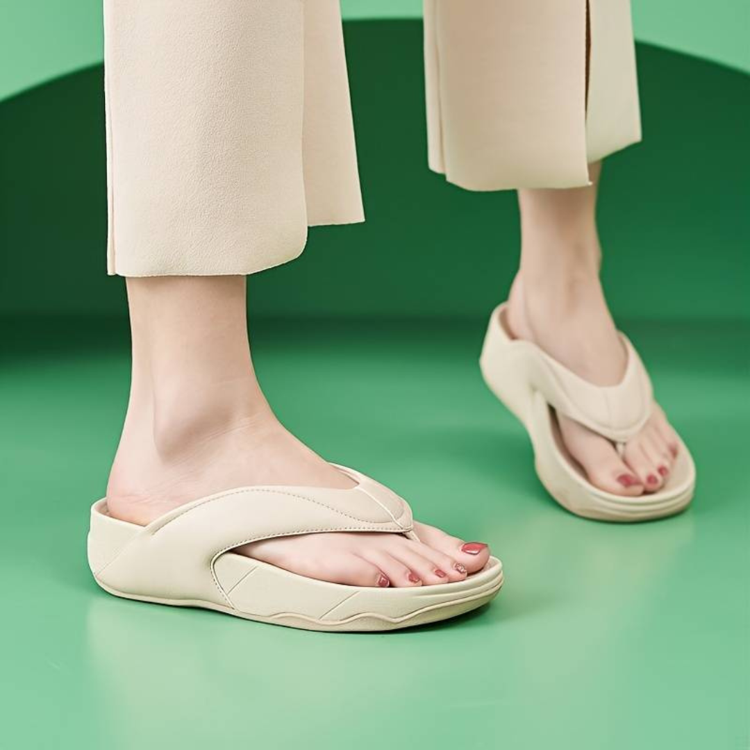 Beige Damen-Sandalen auf grünem Hintergrund, getragen von einer Person in heller Hose. Modische Sommerschuhe, bequem und stilvoll.