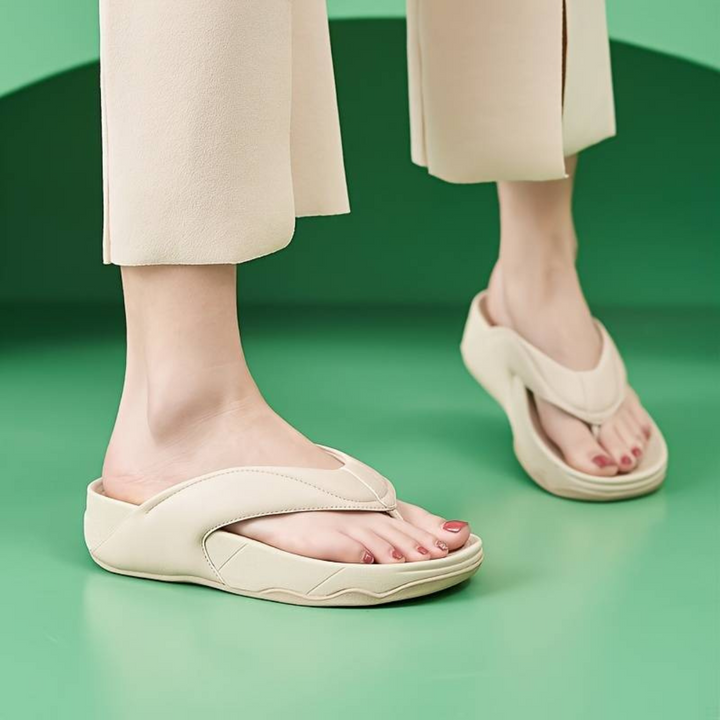 Beige Damen-Sandalen auf grünem Hintergrund, getragen von einer Person in heller Hose. Modische Sommerschuhe, bequem und stilvoll.
