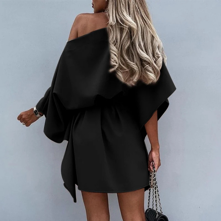 Blonde Frau in schwarzem, schulterfreiem Kleid mit Kettenhandtasche, Rückansicht. Elegante Mode, Abendkleid, stilvoller Look.