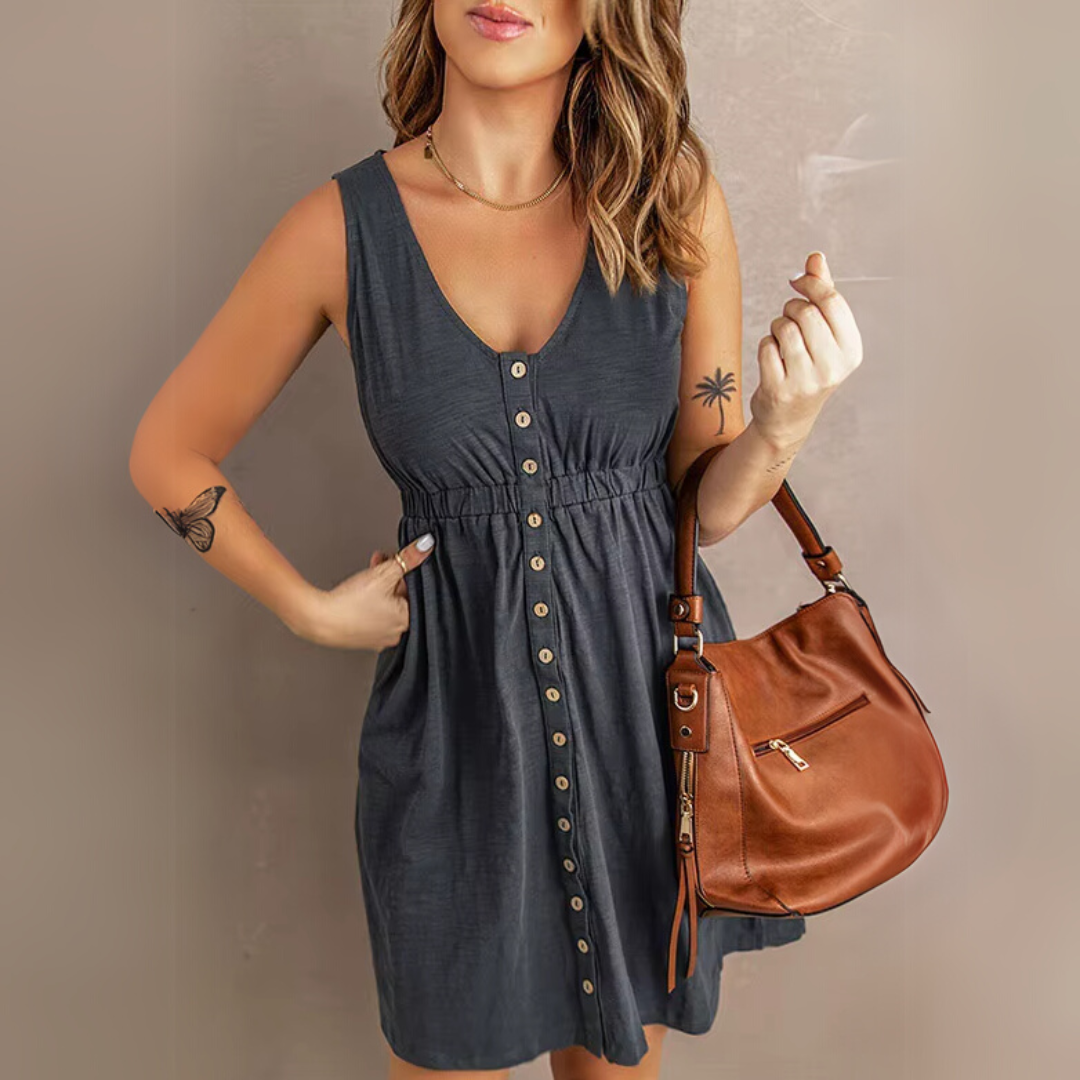 Frau in grauem Sommerkleid mit Knopfleiste, brauner Ledertasche, Tattoos auf Arm und Handgelenk. Modetrend, Damenmode, Sommeroutfit.