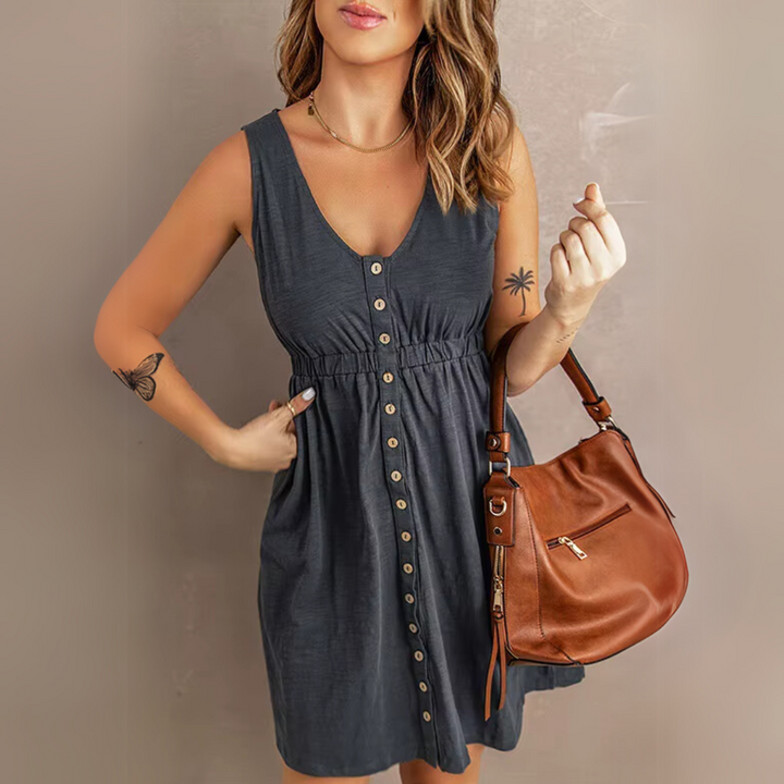 Frau in grauem Sommerkleid mit Knopfleiste, brauner Ledertasche, Tattoos auf Arm und Handgelenk. Modetrend, Damenmode, Sommeroutfit.