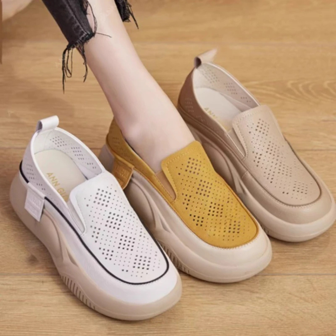 Damen Slip-On Sneaker in Weiß, Gelb und Beige auf Holzboden. Modische, atmungsaktive Freizeitschuhe mit dicker Sohle und perforiertem Design.