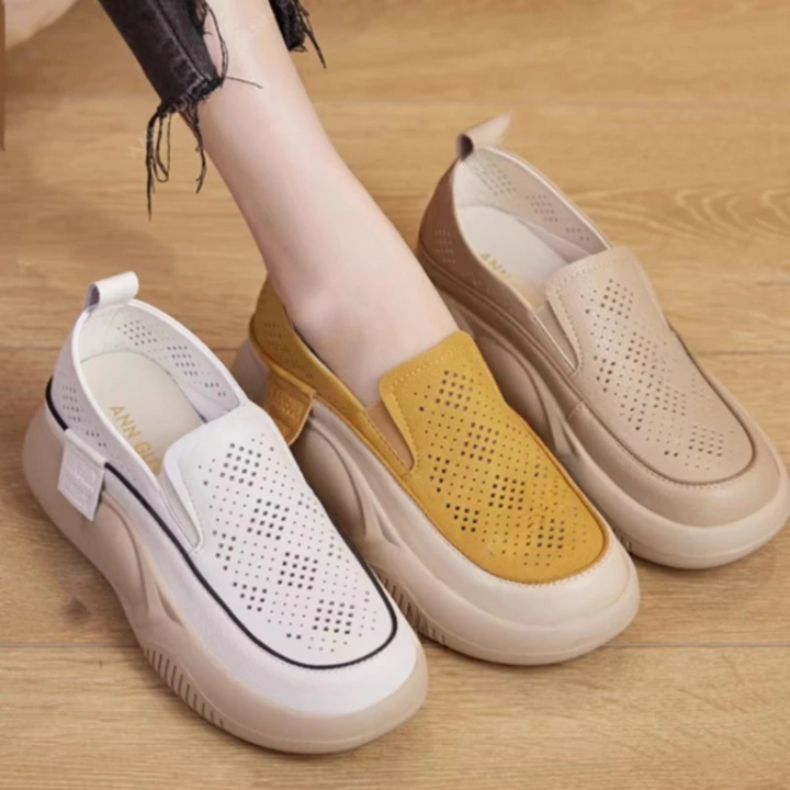 Damen Slip-On Sneaker in Weiß, Gelb und Beige auf Holzboden. Modische, atmungsaktive Freizeitschuhe mit dicker Sohle und perforiertem Design.