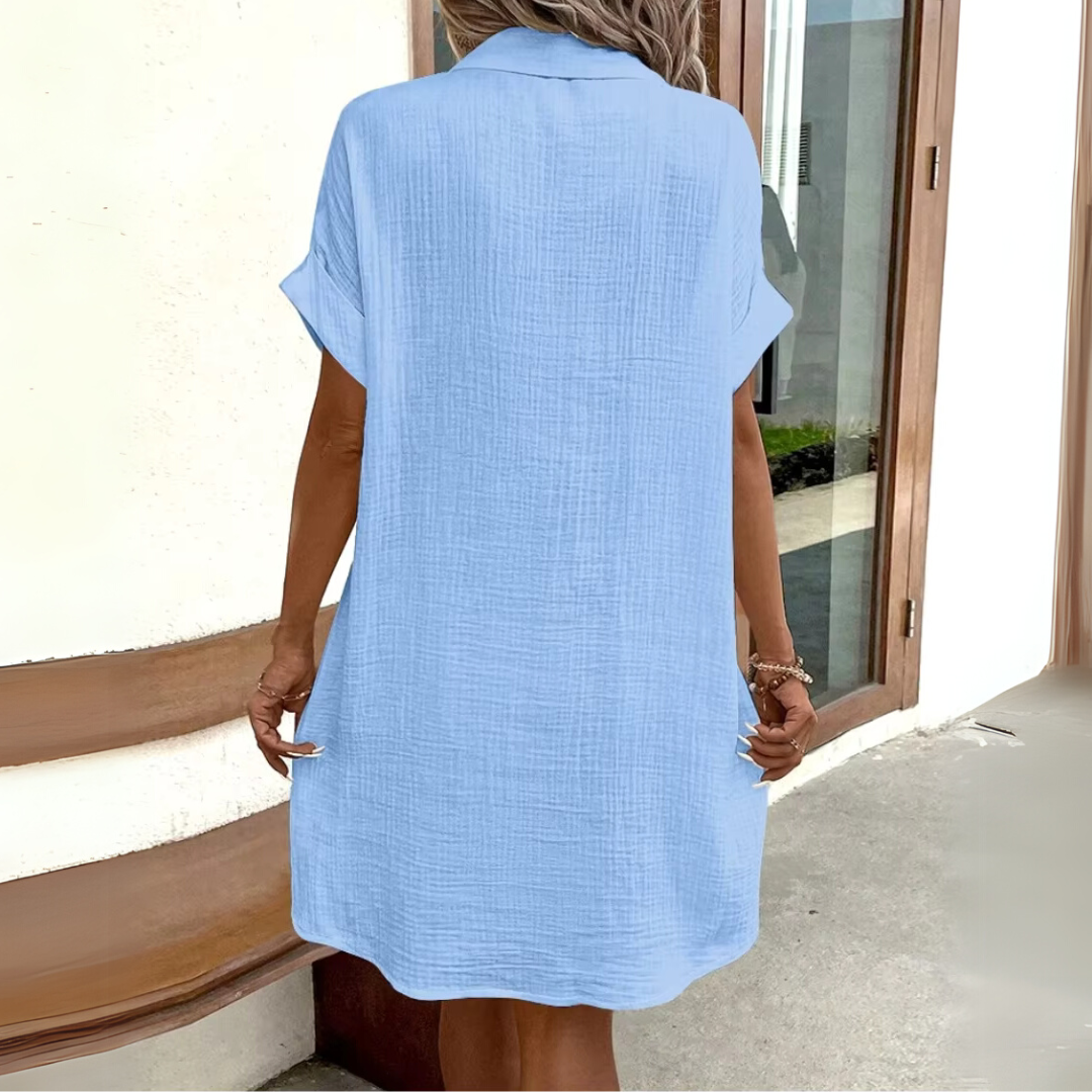 Frau in hellblauem Sommerkleid aus Leinen, steht vor modernem Gebäude. Lässige Mode, Sommerkleid, Leinenkleid, Damenbekleidung, Freizeitlook.