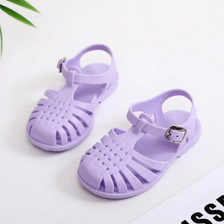 Lila Kinder-Sandalen aus Kunststoff mit Schnalle auf weißem Hintergrund. Sommermode, bequeme Schuhe, atmungsaktiv, rutschfest.