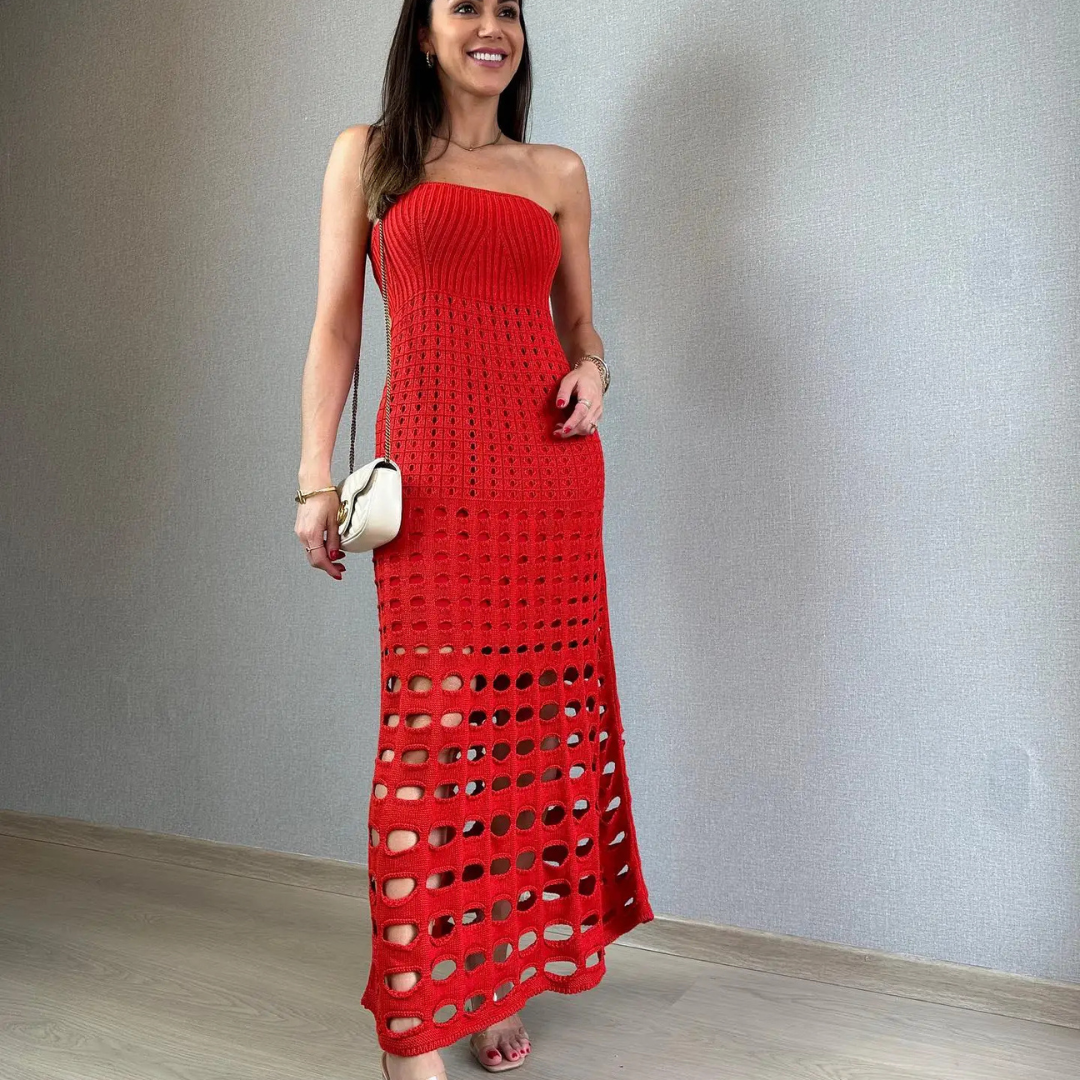 Frau in rotem, schulterfreiem Strickkleid mit Lochmuster, hält weiße Handtasche, steht vor grauer Wand. Elegante Mode, Sommerkleid, Damenbekleidung.