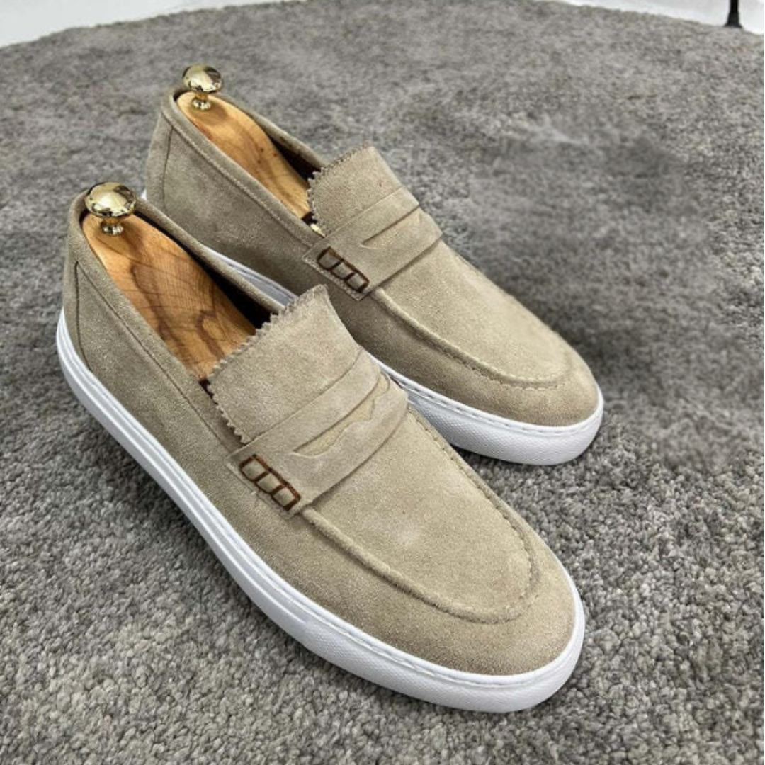 Beige Wildleder-Slipper mit weißer Sohle auf grauem Teppich. Modische Herrenschuhe, elegant und bequem, ideal für Freizeit und Business.