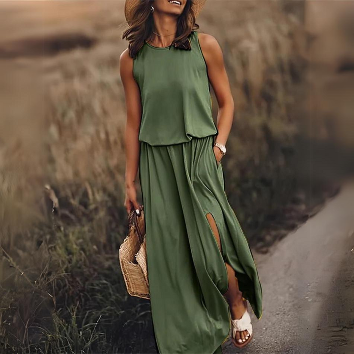Frau in grünem Maxikleid mit Schlitz, Strohhut und Sandalen auf ländlichem Weg. Sommermode, Freizeitkleidung, stilvoller Look.