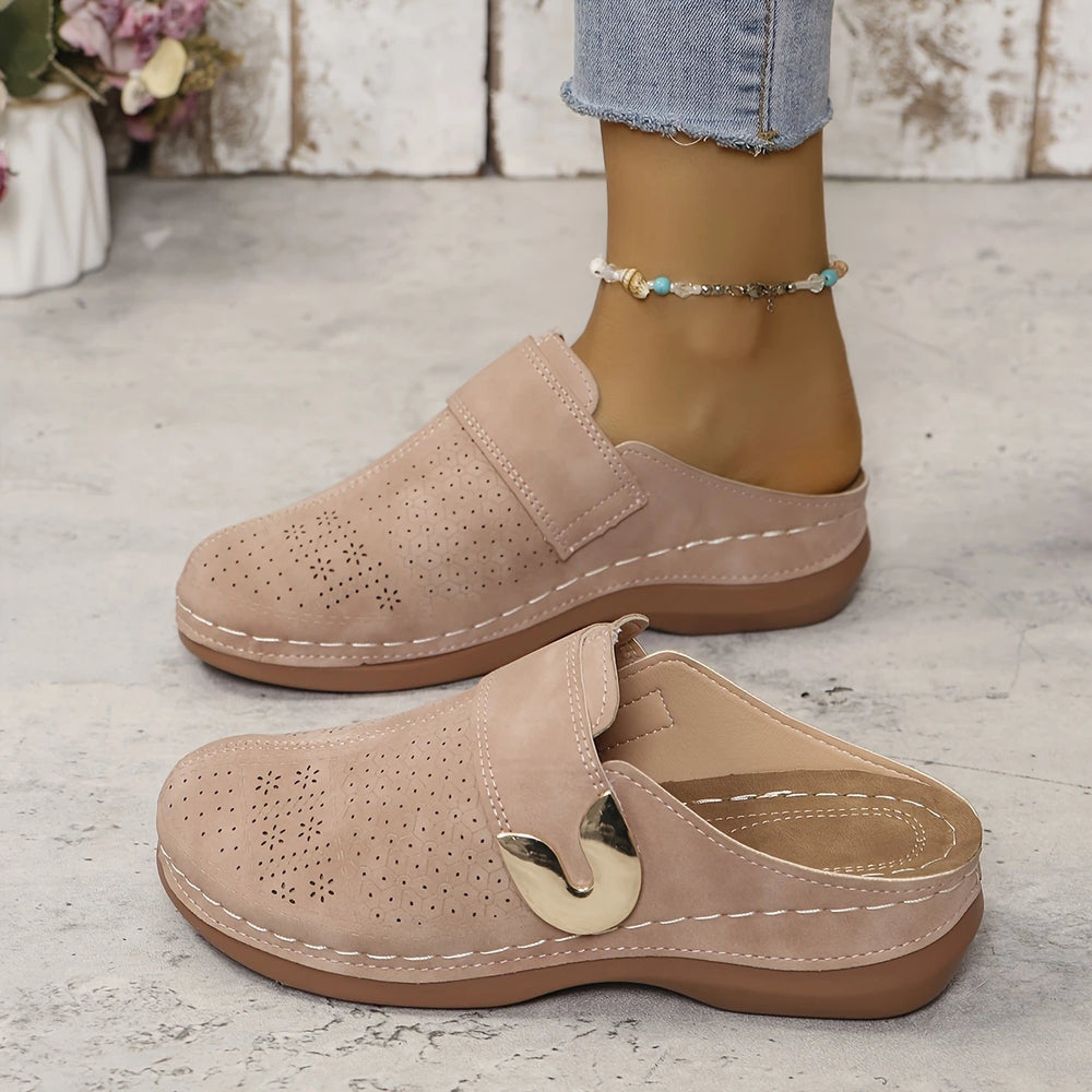 Beige Damen-Clogs mit Lochmuster, goldener Schnalle und bequemer Sohle, getragen mit Jeans. Perfekte Sommerschuhe für Freizeit und Komfort.