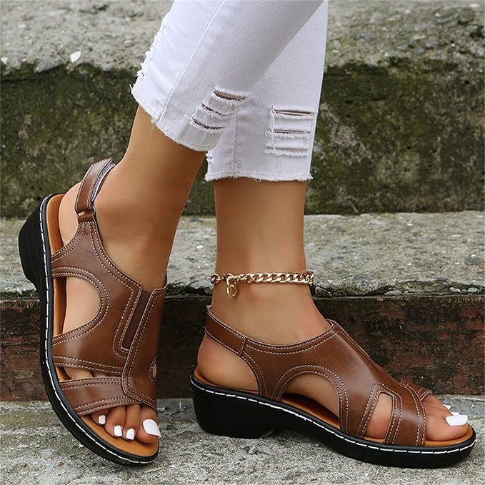 Braune Sandalen mit Keilabsatz an Frauenfüßen, kombiniert mit weißen, zerrissenen Jeans. Modische Sommerschuhe auf Treppe.