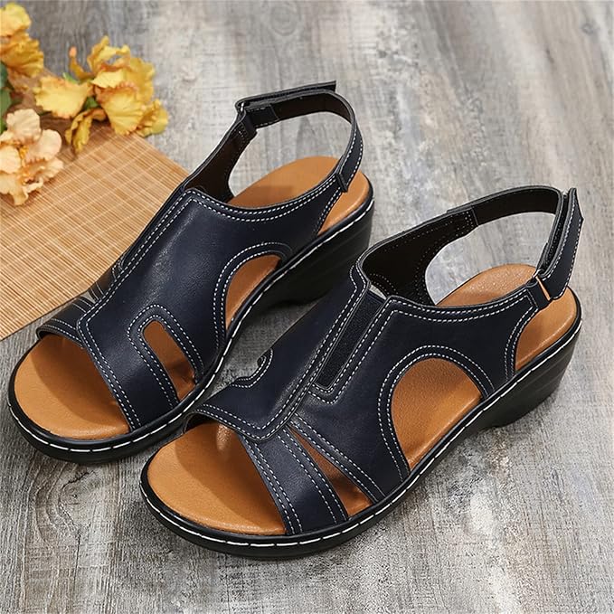 Damen Sandalen mit Keilabsatz, schwarz, aus Leder, mit weißen Nähten, auf Holzboden, neben gelben Blumen. Bequem und modisch für den Sommer.